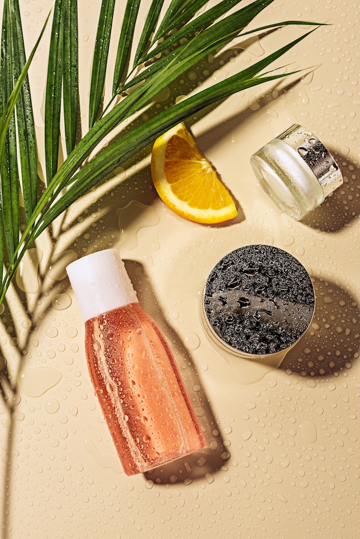 flat lay with skin care products, green palm leaf and orange slice with water drops on beige